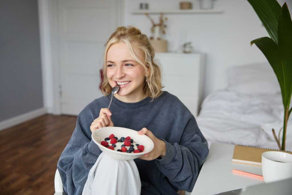 close up portrait smiling cute blond woman eating healthy lunch her room holding bowl with