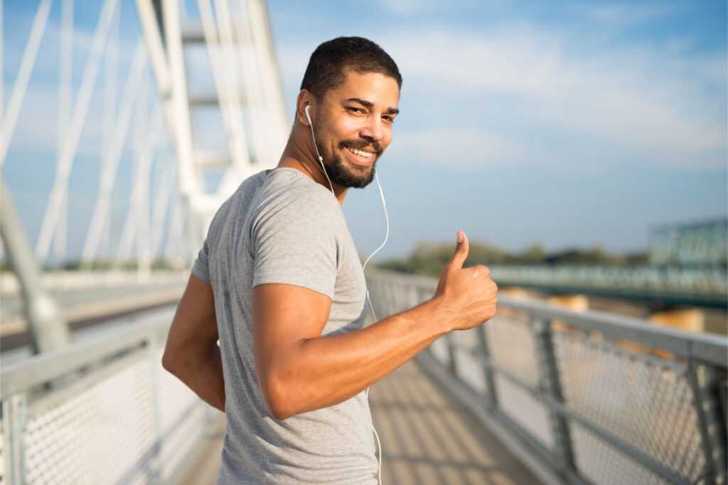 smiling athlete with earphones holding thumbs up ready training