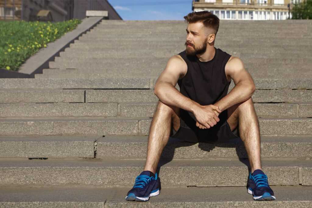 sports people health vitality active lifestyle concept picture handsome young bearded sportswoman with muscular tanned body having break while training outdoors sitting concrete steps