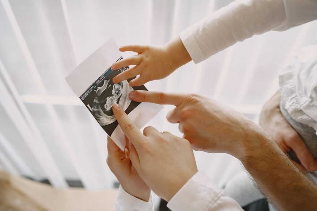 mom dad daughter watching ultrasound picture baby family light clothes family expecting baby